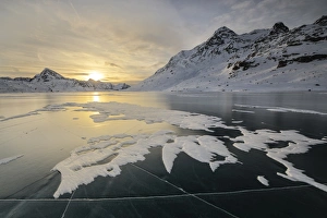 The frozen surface of Lago Bianco framed by snowy peaks at dawn, Bernina Pass, canton of Graubunden The frozen surface of Lago Bianco framed by snowy peaks at dawn, Bernina Pass, canton of Graubunden