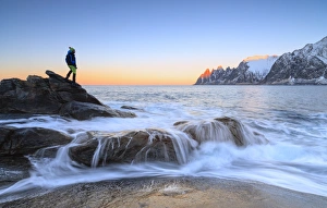 Hiker admires the waves of the icy sea crashing on the rocky cliffs at dawn, Tungeneset Hiker admires the waves of the icy sea crashing on the rocky cliffs at dawn, Tungeneset
