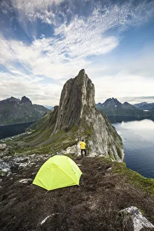 Hiker man with camping tent admiring Mount Segla and fjord from Hesten peak at sunset Hiker man with camping tent admiring Mount Segla and fjord from Hesten peak at sunset