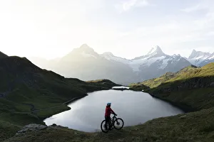 Hiker with mountain bike admiring sunrise over Bachalpsee lake, Grindelwald Hiker with mountain bike admiring sunrise over Bachalpsee lake, Grindelwald