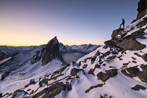 Hiker on peak Hesten admires Mount Segla and the Mefjorden framed by frozen sea at sunrise Hiker on peak Hesten admires Mount Segla and the Mefjorden framed by frozen sea at sunrise