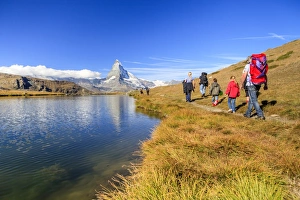 Hikers walking on the path beside the Stellisee with the Matterhorn reflected, Zermatt Hikers walking on the path beside the Stellisee with the Matterhorn reflected, Zermatt