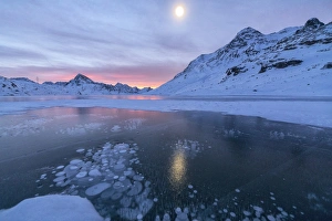 Ice bubbles frame the frozen Lago Bianco at dawn, Bernina Pass, canton of Graubunden Ice bubbles frame the frozen Lago Bianco at dawn, Bernina Pass, canton of Graubunden