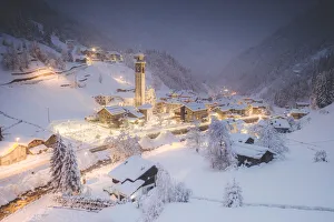 Illuminated village of Gerola Alta and frozen river covered with snow during winter dusk Illuminated village of Gerola Alta and frozen river covered with snow during winter dusk