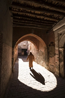 Local man dressed in traditional djellaba walking through archway in a street in the Kasbah Local man dressed in traditional djellaba walking through archway in a street in the Kasbah