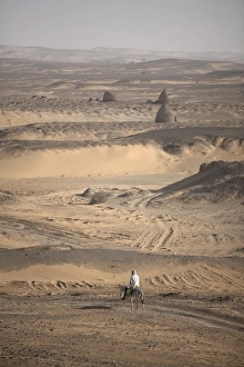 A man on mule-back traverses the desert around the A man on mule-back traverses the desert around the