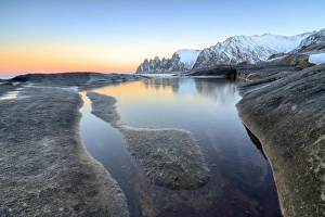 Orange sky at sunset reflected on snowy peaks and the frozen sea surrounded by rocks Tungeneset Orange sky at sunset reflected on snowy peaks and the frozen sea surrounded by rocks Tungeneset