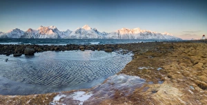Panorama of frozen sea and snowy peaks at dawn surrounded by rocks covered with ice Panorama of frozen sea and snowy peaks at dawn surrounded by rocks covered with ice