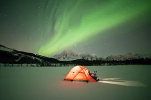 Photographer in a tent lit up by Northern Lights (aurora borealis) and starry sky Photographer in a tent lit up by Northern Lights (aurora borealis) and starry sky