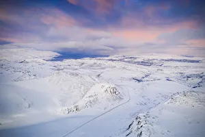 Pink sky at sunrise over Tanafjordveien road crossing the snow capped mountains, Tana Pink sky at sunrise over Tanafjordveien road crossing the snow capped mountains, Tana