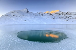 The Piz Cambrena illuminated by the sun reflecting in a pool surrounded by ice at the Bernina, Graubunden, Swiss Alps, Switzerland, Europe The Piz Cambrena illuminated by the sun reflecting in a pool surrounded by ice at the Bernina, Graubunden, Swiss Alps, Switzerland, Europe