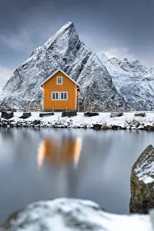 Rorbu in the snow at foot of Olstind mountain overlooking the Arctic Sea, Sakrisoy, Reine, Nordland, Lofoten Islands Rorbu in the snow at foot of Olstind mountain overlooking the Arctic Sea, Sakrisoy, Reine, Nordland, Lofoten Islands