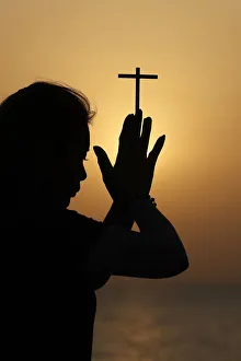 Silhouette of faithful religious woman praying with Christian cross at sunset Silhouette of faithful religious woman praying with Christian cross at sunset
