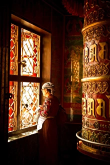 A Tibetan woman stands next to a large prayer wheel of the temple of Boudhanath Stupa A Tibetan woman stands next to a large prayer wheel of the temple of Boudhanath Stupa