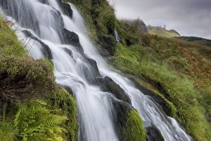 Waterfall cascading down grassy slope with Old Man of Storr in background Waterfall cascading down grassy slope with Old Man of Storr in background