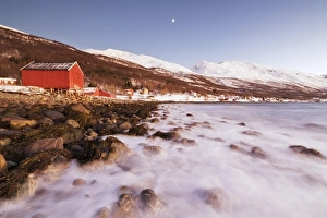 Waves of cold sea crashing on the rocks and typical wooden huts called Rorbu, Djupvik Waves of cold sea crashing on the rocks and typical wooden huts called Rorbu, Djupvik