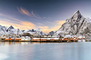 Winter sunset over snowcapped mountains and Sakrisoy village by the frozen sea, Reine, Nordland, Lofoten Islands Winter sunset over snowcapped mountains and Sakrisoy village by the frozen sea, Reine, Nordland, Lofoten Islands