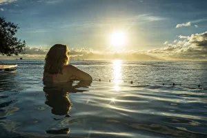 Woman enjoying the sunset in a swimming pool with Moorea in the background, Papeete Woman enjoying the sunset in a swimming pool with Moorea in the background, Papeete