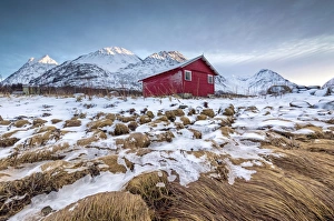 Wood hut framed by rocks covered with grass and ice with snowy peaks in the background Wood hut framed by rocks covered with grass and ice with snowy peaks in the background