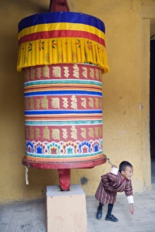 Prints of Young boy pulling a prayer wheel, Jakar Dzong, Castle of the White Bird, Jakar, Bumthang, Chokor Valley, Bhutan, Asia Bhutan Prints: Bhutanese Landscape Print - Young Boy Pulling a Prayer Wheel
