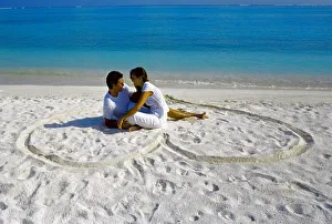 Young couple on beach sitting in a heart shaped imprint on the sand, Maldives Young couple on beach sitting in a heart shaped imprint on the sand, Maldives