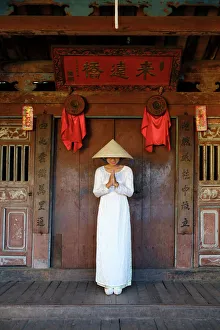 A young woman in a Non La conical hat and a traditional Ao Dai dress in the historical centre A young woman in a Non La conical hat and a traditional Ao Dai dress in the historical centre