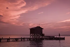 Belize, Tobaco Caye, Man on pier at sunset Belize, Tobaco Caye, Man on pier at sunset