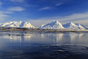 The blue sky and snow capped mountains are reflected in the frozen water Breivikeidet The blue sky and snow capped mountains are reflected in the frozen water Breivikeidet