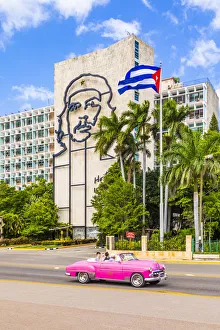A classic car driving in front of a building with an outline of Che Guevara A classic car driving in front of a building with an outline of Che Guevara