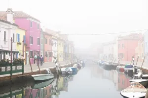 Colorful houses in Burano with canal and moored boats in the fog, Venice, Venetian lagoon Colorful houses in Burano with canal and moored boats in the fog, Venice, Venetian lagoon