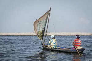 Abomey Collection: two colorfully dressed local women in wooden sailing canoe on the lake