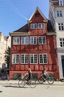 Cyclists pass an old red house in Central Copenhagen, Copenhagen, Denmark Cyclists pass an old red house in Central Copenhagen, Copenhagen, Denmark
