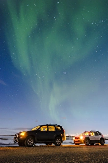 Iceland, Europe. Cars with lights on at night under a starry sky and the northern lights Iceland, Europe. Cars with lights on at night under a starry sky and the northern lights