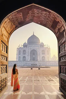 India, a beautiful woman in a red and yellow sari in front of the Taj Mahal at sunrise India, a beautiful woman in a red and yellow sari in front of the Taj Mahal at sunrise