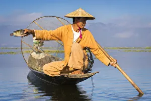 Intha fisherman with a traditional conical fishing net showing fish against clear sky Intha fisherman with a traditional conical fishing net showing fish against clear sky