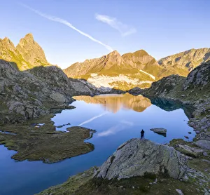 A lonely man admiring a sunrise at Lago Leit with Pizzo Prevat reflecting on it A lonely man admiring a sunrise at Lago Leit with Pizzo Prevat reflecting on it