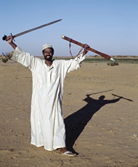 A Nubian man displays his sword at an oasis in the A Nubian man displays his sword at an oasis in the