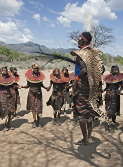 A Pokot warrior wearing a cheetah skin jumps high in the air surrounded by young women to A Pokot warrior wearing a cheetah skin jumps high in the air surrounded by young women to
