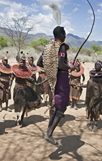A Pokot warrior wearing a leopard skin jumps high in the air surrounded by women to A Pokot warrior wearing a leopard skin jumps high in the air surrounded by women to