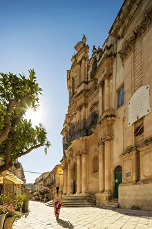 Scicli, Sicily. A woman walking in front of San Giovanni Evangelista church on a sunny Scicli, Sicily. A woman walking in front of San Giovanni Evangelista church on a sunny