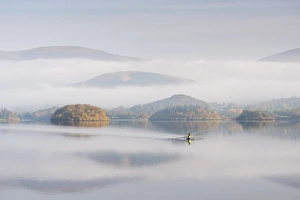 Single sculler rowing across a misty Derwent Water at dawn, Lake District, Cumbria, England