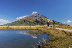 Two tourists hiking at Taranaki volcano in New Zealand northern island reflecting in a Two tourists hiking at Taranaki volcano in New Zealand northern island reflecting in a