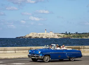 Vintage car at El Malecon with El Morro Castle and Lighthouse in the background, Havana Vintage car at El Malecon with El Morro Castle and Lighthouse in the background, Havana