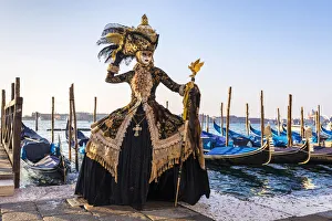 A woman in a magnificent costume poses in front of Gondolas during the Venice Carnival A woman in a magnificent costume poses in front of Gondolas during the Venice Carnival