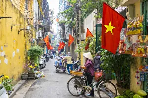 Woman pusing a bicycle through an alleyway lined with red Vietnamese flags, Hoan Woman pusing a bicycle through an alleyway lined with red Vietnamese flags, Hoan