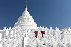 Two young Buddhist monks stand on the white walls of Hsinbyume Pagoda holding red Two young Buddhist monks stand on the white walls of Hsinbyume Pagoda holding red