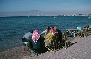 JORDAN, Aqaba Group of men playing backgammon on shore of beach with Eliat JORDAN, Aqaba Group of men playing backgammon on shore of beach with Eliat