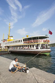 Turkey, Istanbul, Man fishing on quayside, and passenger ferry in Karakoy Cruise Terminal, Bosphorus Strait Turkey, Istanbul, Man fishing on quayside, and passenger ferry in Karakoy Cruise Terminal, Bosphorus Strait