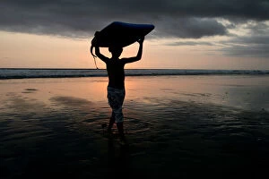 Images Dated 9th October 2005: A boy carries his boogie board near Kuta beach on the Indonesian resort island of Bali