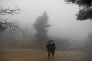 A couple holds an umbrella as they walk on the street on a foggy day in Jerusalem A couple holds an umbrella as they walk on the street on a foggy day in Jerusalem